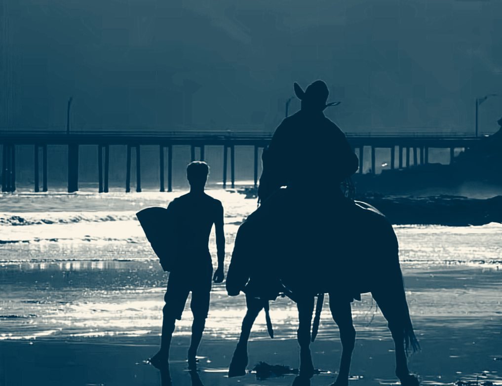 A surfer and a cowboy on horseback walking the shoreline at dusk